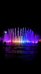 Colorful fountain display illuminates urban park at night with vibrant lights