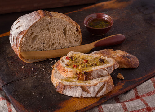 Partially sliced loaf of artisan sourdough bread with olive oil dipping sauce on a rustic cutting board; copy space