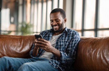 Relaxed man smiles while checking his phone on a leather couch.