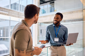 Happy black businessman using laptop while talking to his colleague in office.