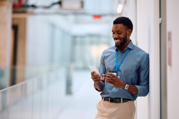 Happy black entrepreneur using cell phone during his coffee break in office.