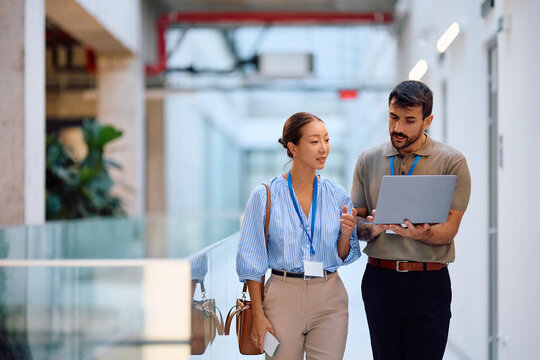 Business coworkers using laptop in hallway of office building.