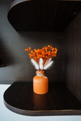 A small, beautifully crafted orange vase that is filled with a selection of dried flowers is...