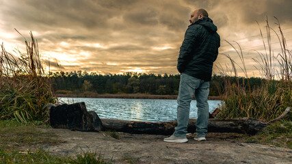 A lonely man stands on the shore of a lake during sunset