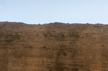 Earthen wall shows texture and pattern against a pale sky, creating an abstract, natural background...