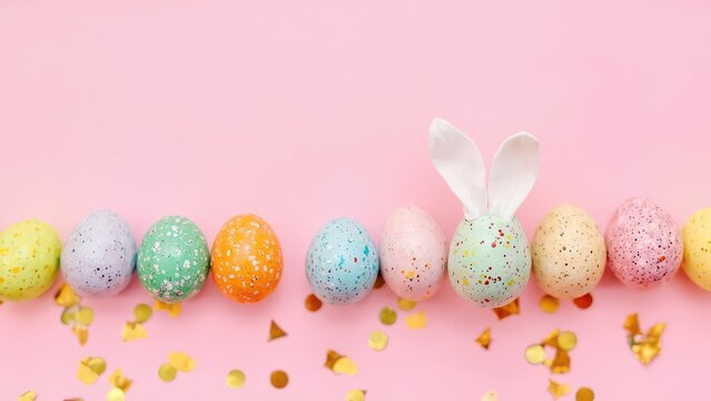 Colorful Easter Eggs with Bunny Ears on Pink Background. A vibrant and cheerful Easter flat lay featuring a row of speckled Easter eggs in various pastel colors on a light pink background. 