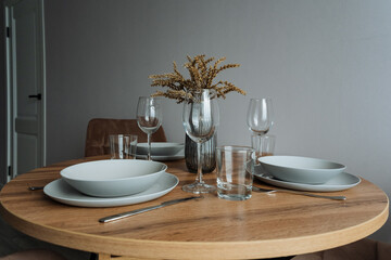 A beautifully crafted wooden table adorned with plates, bowls, and glasses, accompanied by a delightful vase of flowers sitting right on top of it, creating a charming display