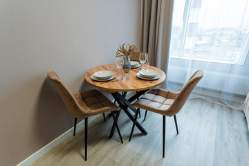 In a cozy living room, there is a small wooden table accompanied by matching chairs situated neatly beside a window, creating a warm and inviting atmosphere for relaxation and gatherings