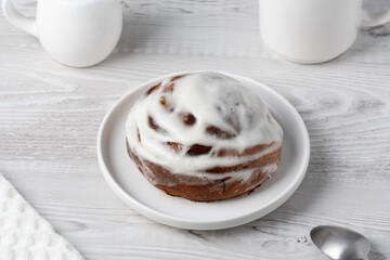 Cinnamon bun in white plate with coffee and napkin on white table