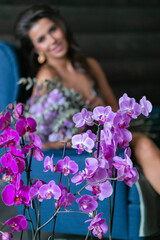 beautiful mulatto woman sits in a blue chair with a bouquet of fresh flowers