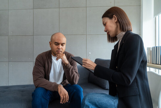 Asian man consulting with asian woman psychologist at mental health clinic. psychologist taking notes and talking with male patient with depression.