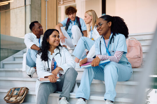 Happy female medical students talking while relaxing on staircase at university.