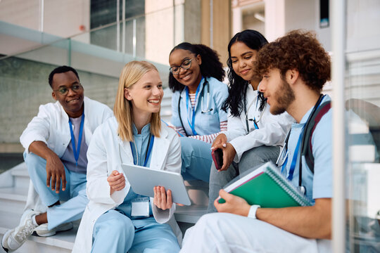 Happy medical student and her colleagues using touchpad while relaxing at university.