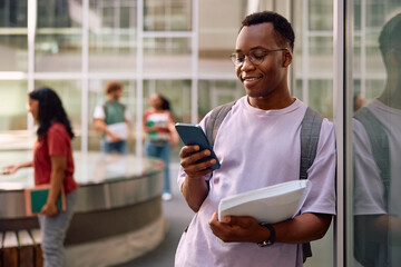 Happy black student using smart phone at university campus.