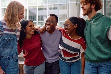 Group of happy college friends having fun while standing embraced at campus.