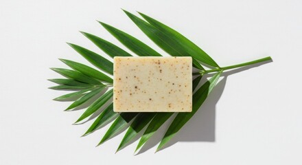 A bar of soap with specks rests on a green palm leaf against a white background