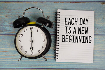 Each day is a New Beginning text written on notepad with alarm clock on wooden background