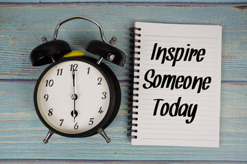 Inspire Someone Today text written on notepad with alarm clock on wooden background