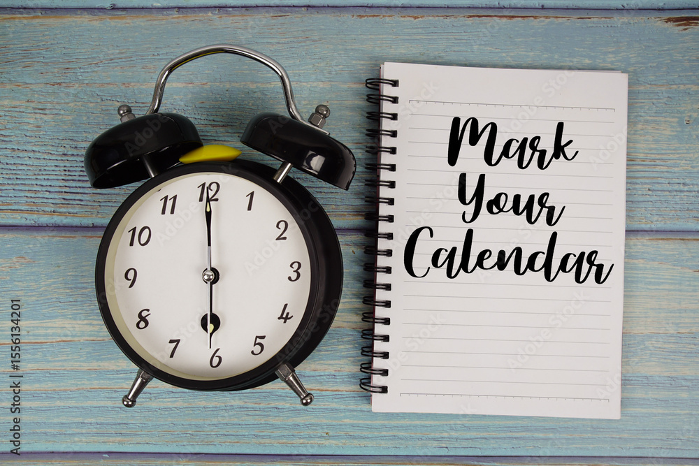 Poster mark your calendar text written on notepad with alarm clock on wooden background