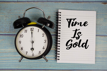 Time is Gold text written on notepad with alarm clock on wooden background