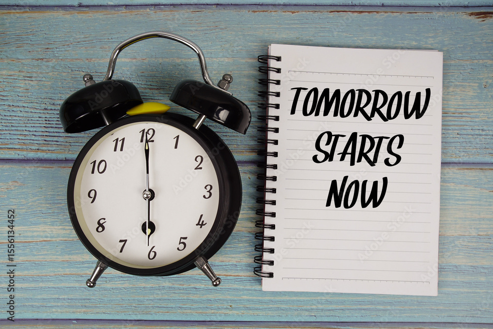 Poster tomorrow starts now text written on notepad with alarm clock on wooden background