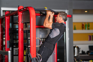  man strengthening his muscles by doing pull-up on horizontal bar in a fitness center
