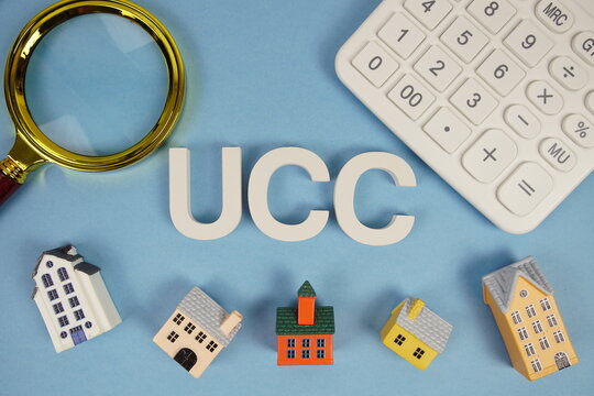 UCC abbreviation of Uniform Commercial Code alphabet letters with house model, magnifying glass and calculator on blue background