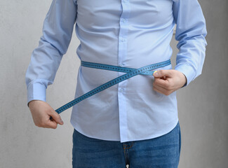 An overweight man measures the circumference of his protruding, swollen belly.