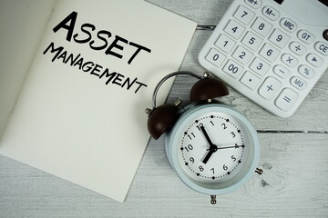 Asset Management text on paper notebook page with alarm clock and calculator on wooden background