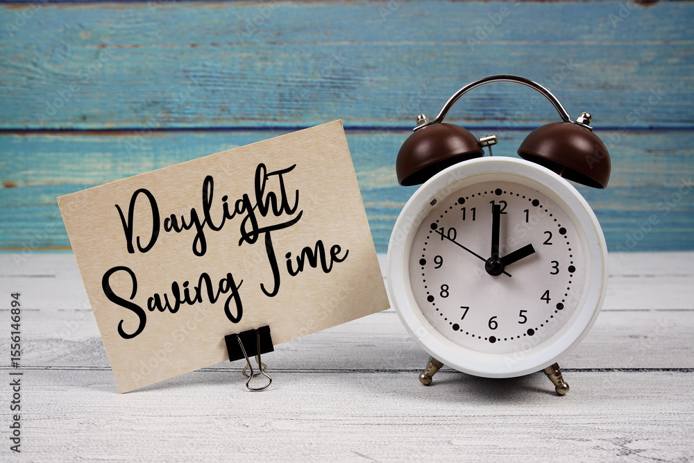 Poster daylight saving time text written on paper card with alarm clock on wooden background