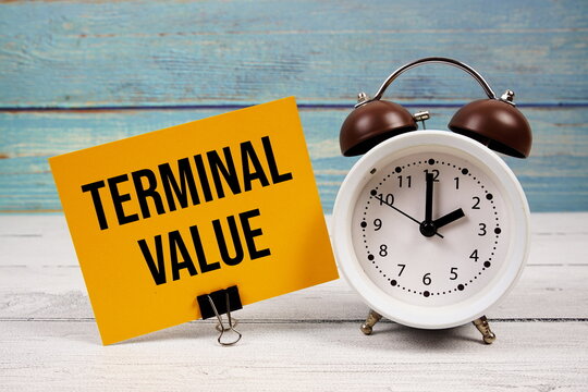 Terminal Value text written on paper card with alarm clock on wooden background