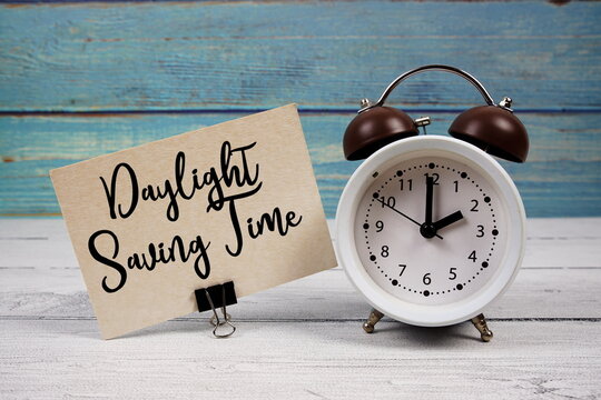 Daylight Saving Time text written on paper card with alarm clock on wooden background