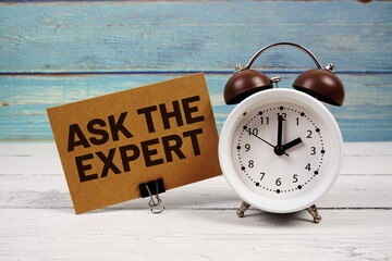 Ask The Expert text written on paper card with alarm clock on wooden background