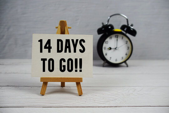 14 Days To Go! text with easel and alarm clock on wooden background