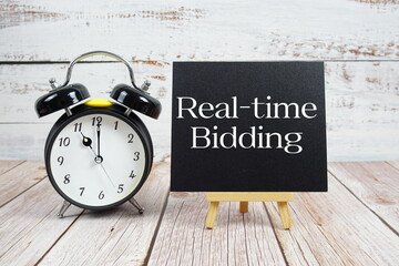 Real-time Bidding text with easel and alarm clock on wooden background