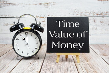 Time Value of Money text with easel and alarm clock on wooden background