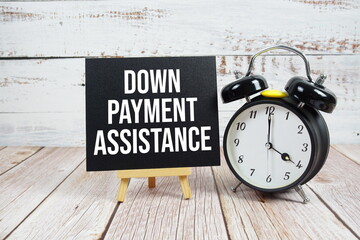 Down Payment Assistance text with easel and alarm clock on wooden background
