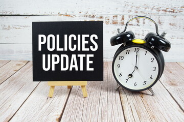 Policies Update text with easel and alarm clock on wooden background