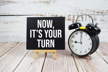 Now,it's Your Turn text with easel and alarm clock on wooden background