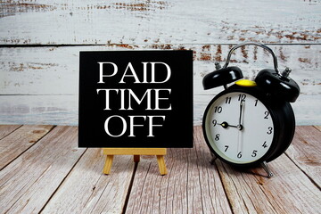 Paid Time Off text with easel and alarm clock on wooden background