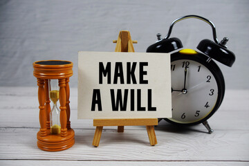 Make a Will text with hourglass and alarm clock on wooden background