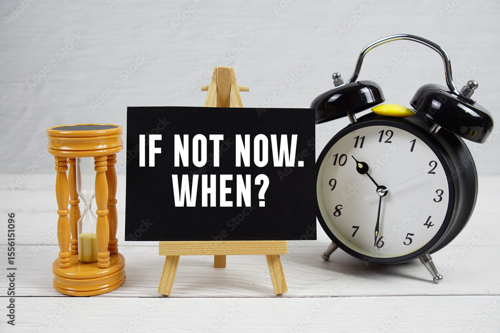 Poster if not now. when? text with hourglass and alarm clock on wooden background