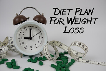 Diet Plan For Weight Loss text with medicine, alarm clock and measuring tape on white background