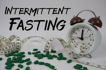 Intermittent Fasting text with medicine, alarm clock and measuring tape on white background