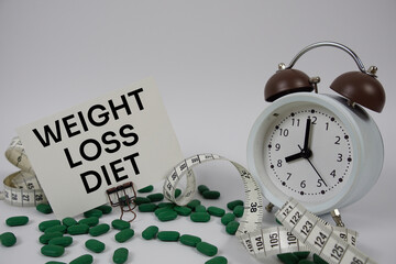 Weight Loss Diet text with medicine, alarm clock and measuring tape on white background