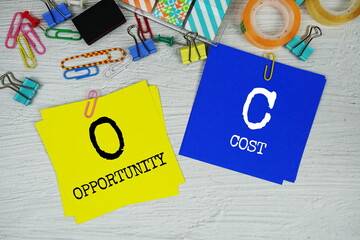 OC - Opportunity Cost text on stick note with stationery on concrete background