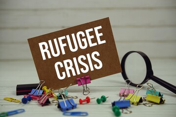 Refugee Crisis text on paper card with magnifying glass and stationary on wooden background