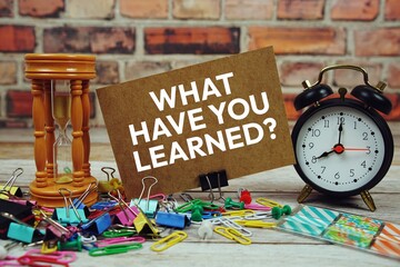 What have you Learned? text on paper card with alarm clock and stationary on wooden background