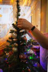 Decorates Christmas tree with colorful ornaments while family shares joyful moments indoors in warm lighting