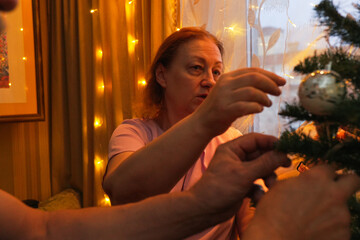 Woman decorates Christmas tree with ornaments in cozy living room during festive holiday season